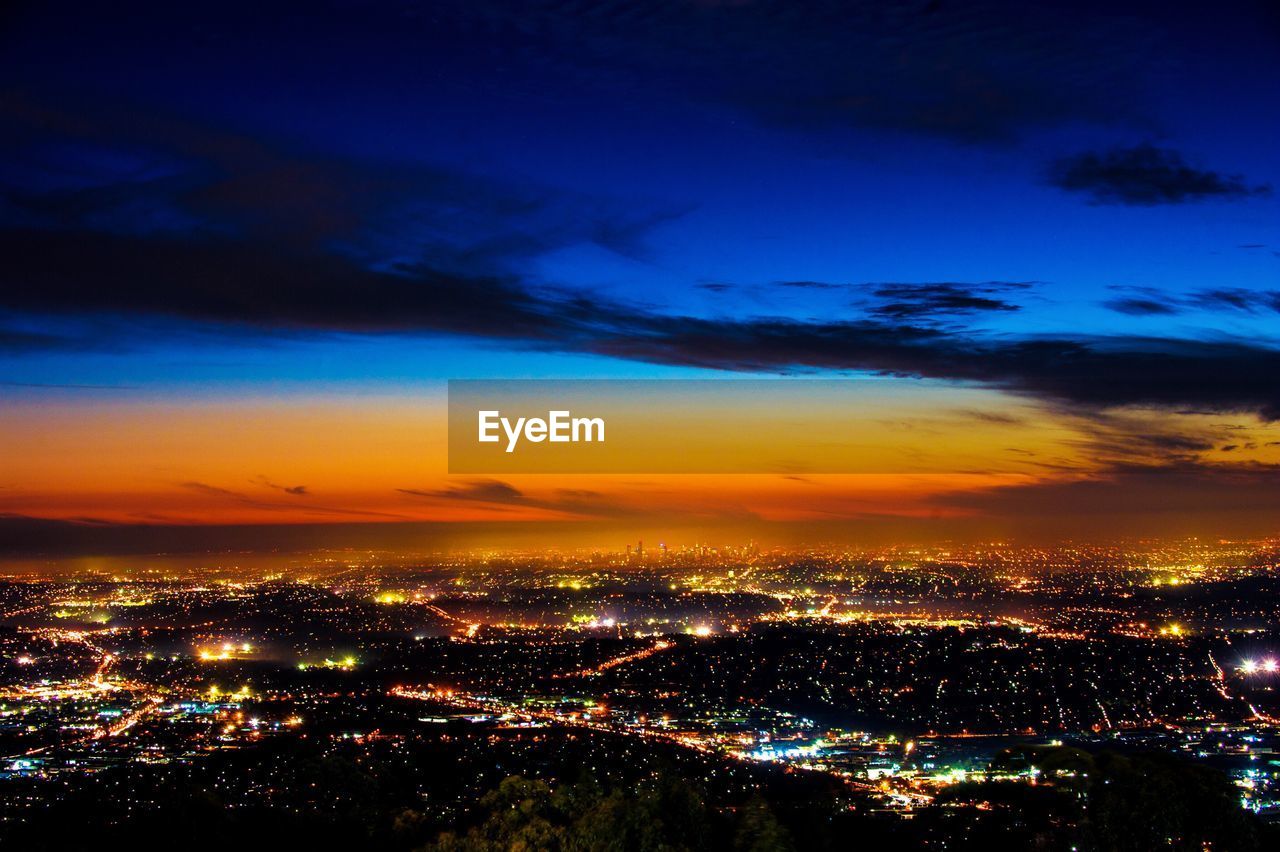 Aerial view of illuminated cityscape against sky at sunset