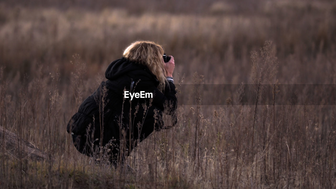 Woman crouching while photographing on field