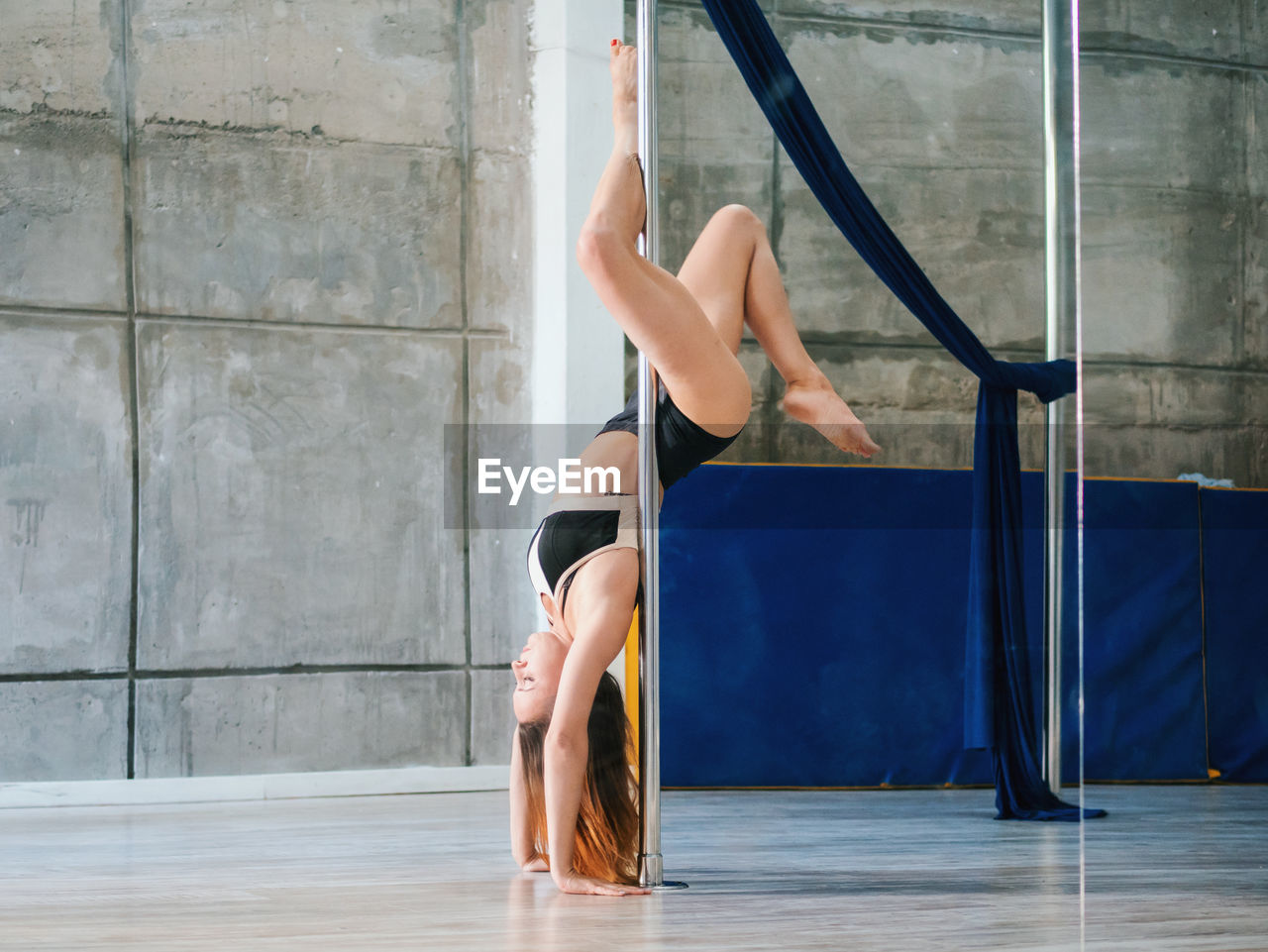 Side view full length of sensuous woman practicing pole dance in studio