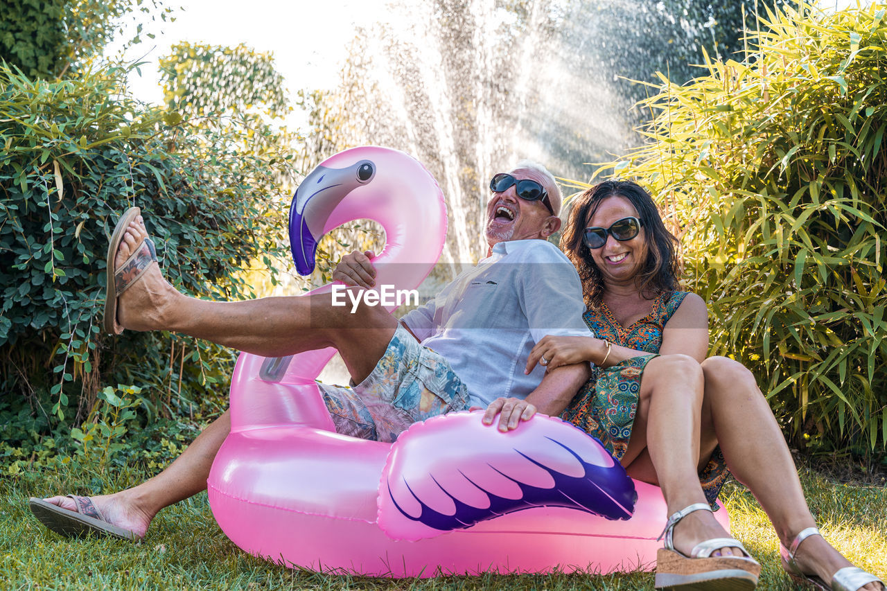 side view of young woman wearing sunglasses while sitting in bikini standing against trees