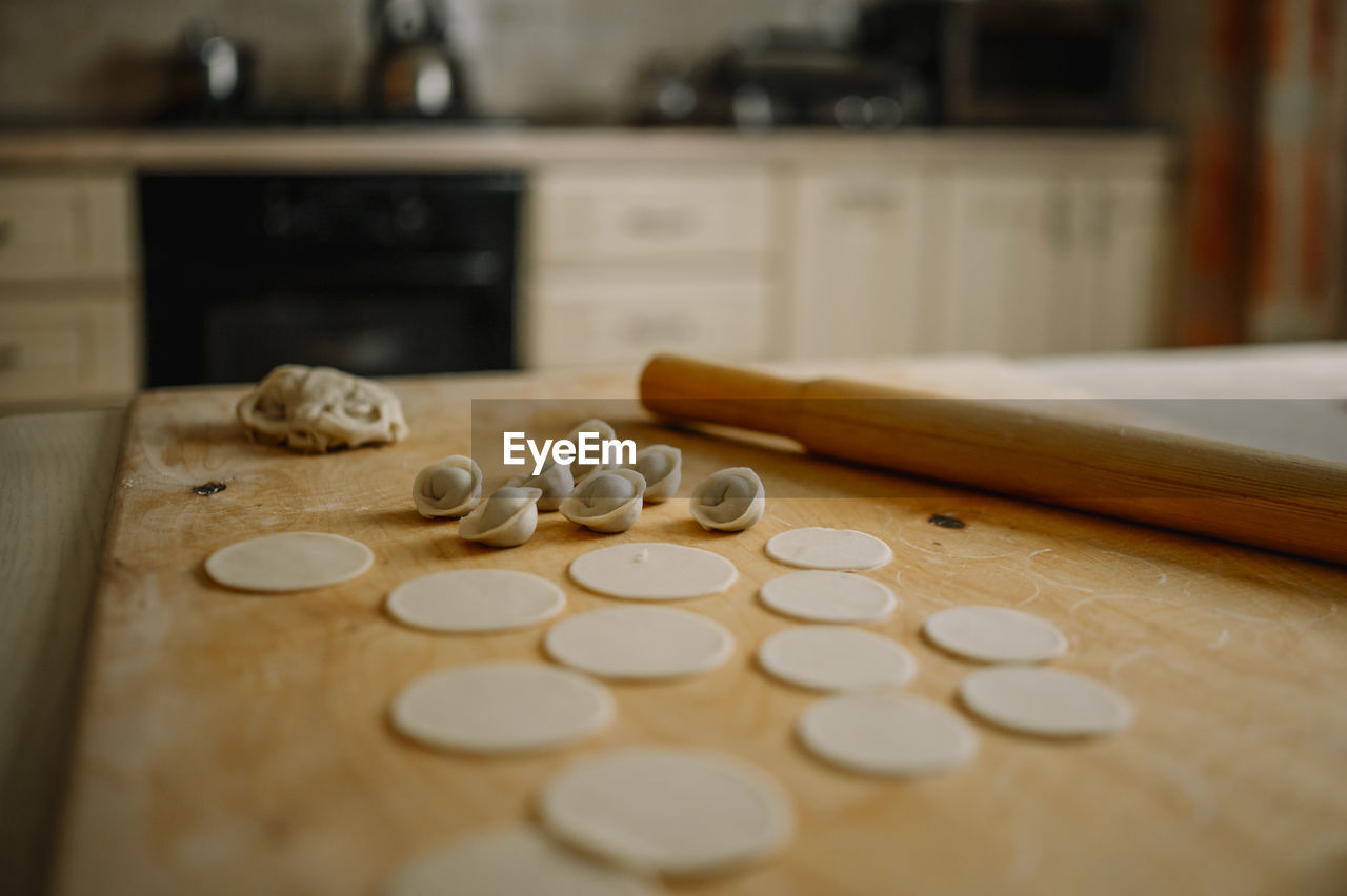 Rolling pin by dumplings on cutting board in kitchen at home