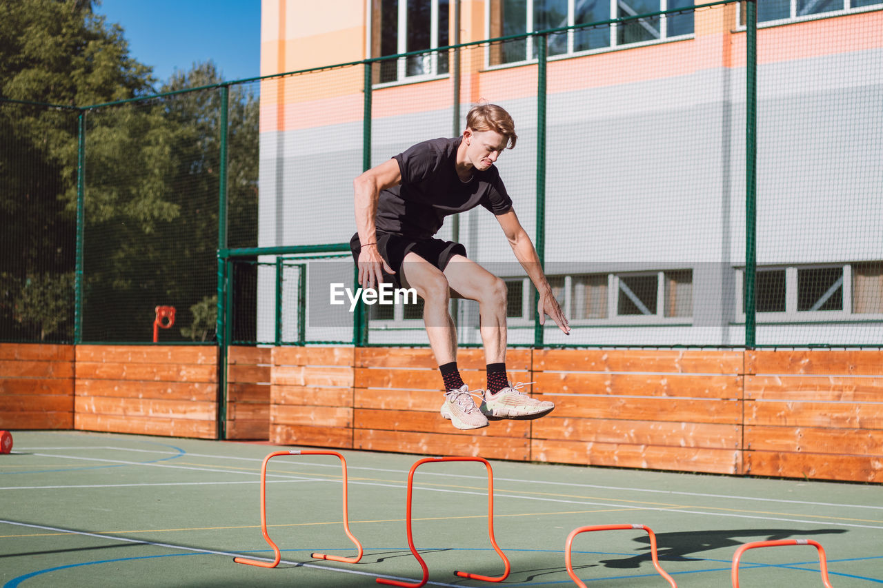 Blond boy in sportswear jumps over red obstacles to improve lower body dynamics