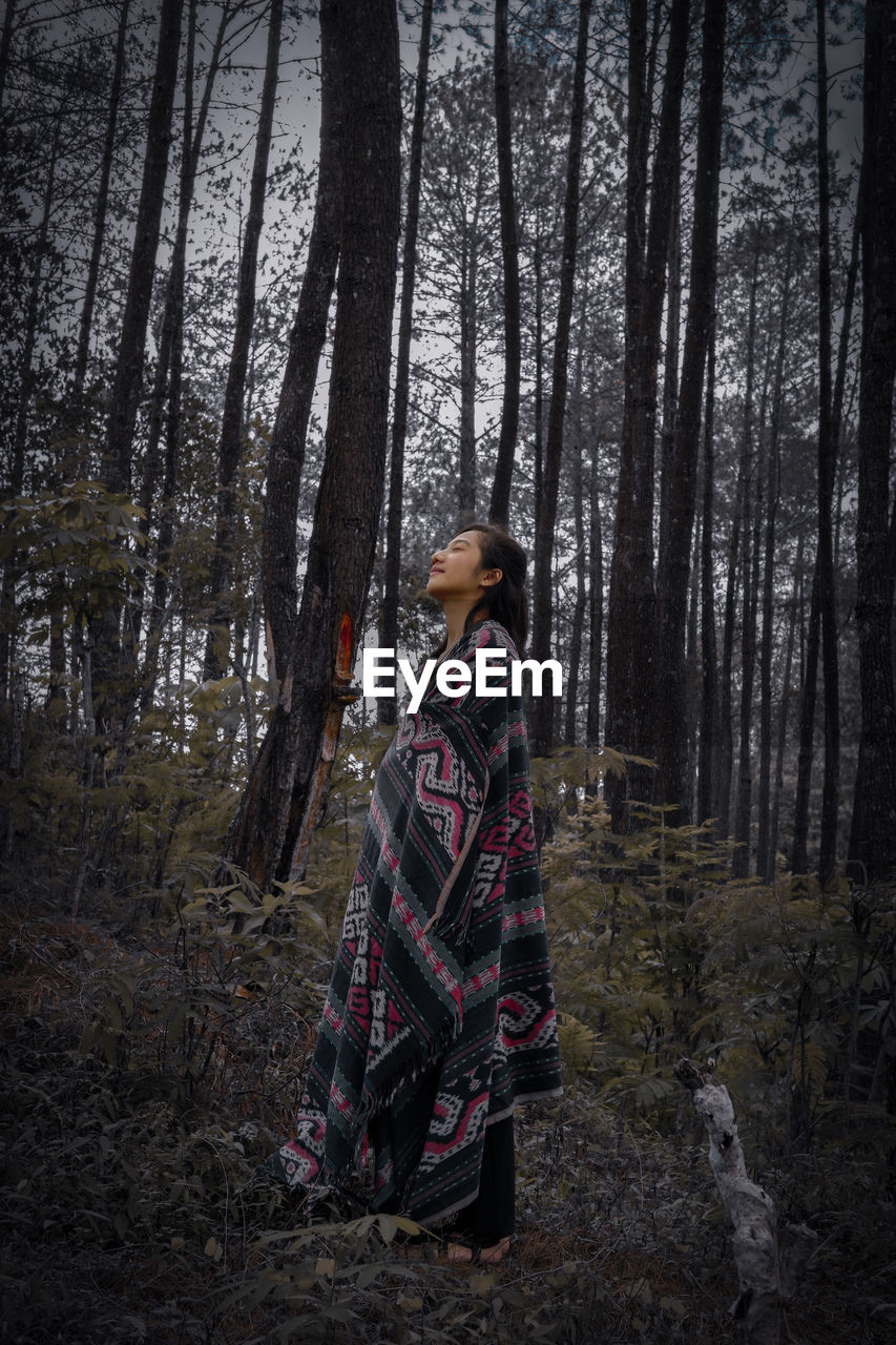 Side view of woman standing against trees in forest