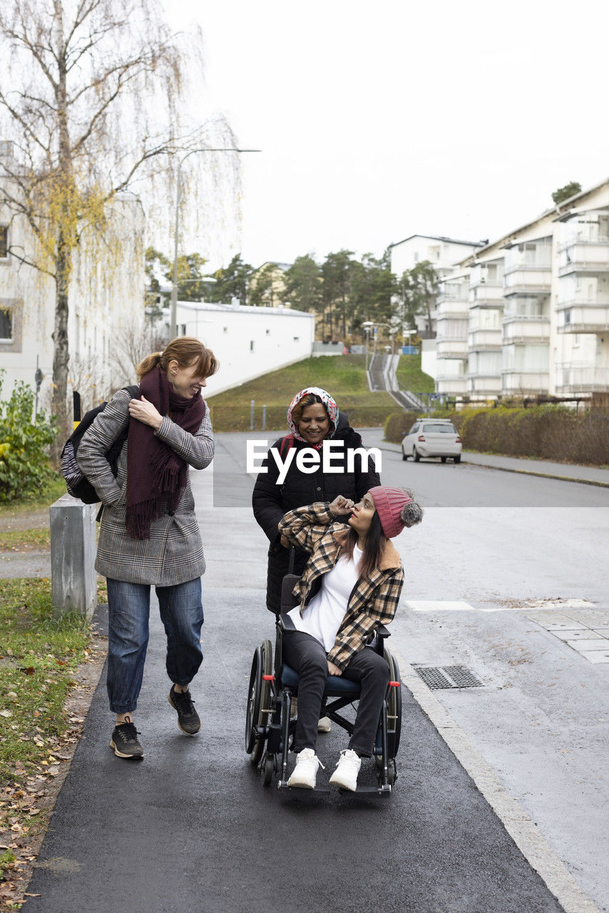 Mother and nurse talking to woman sitting on wheelchair while walking at sidewalk