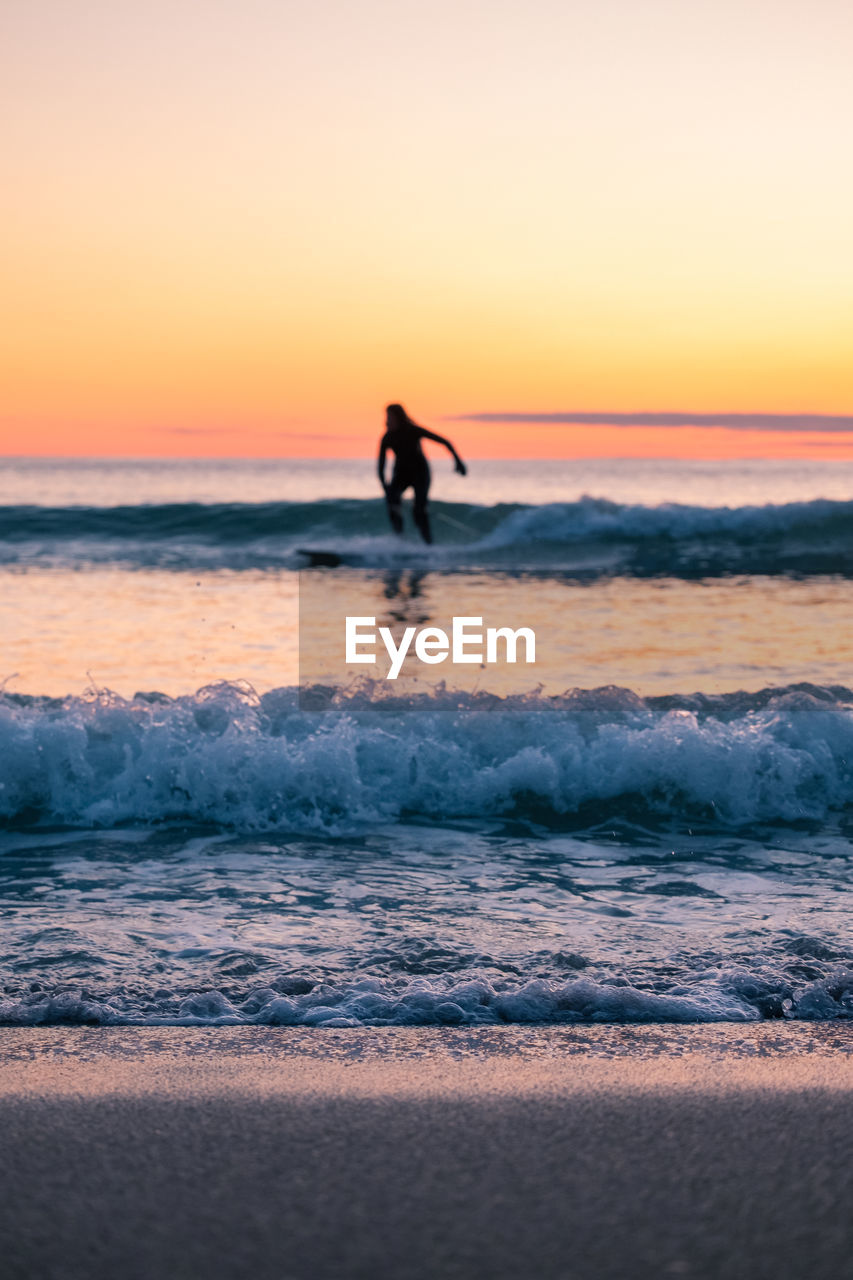 Silhouette woman surfing on sea against clear sky during sunset