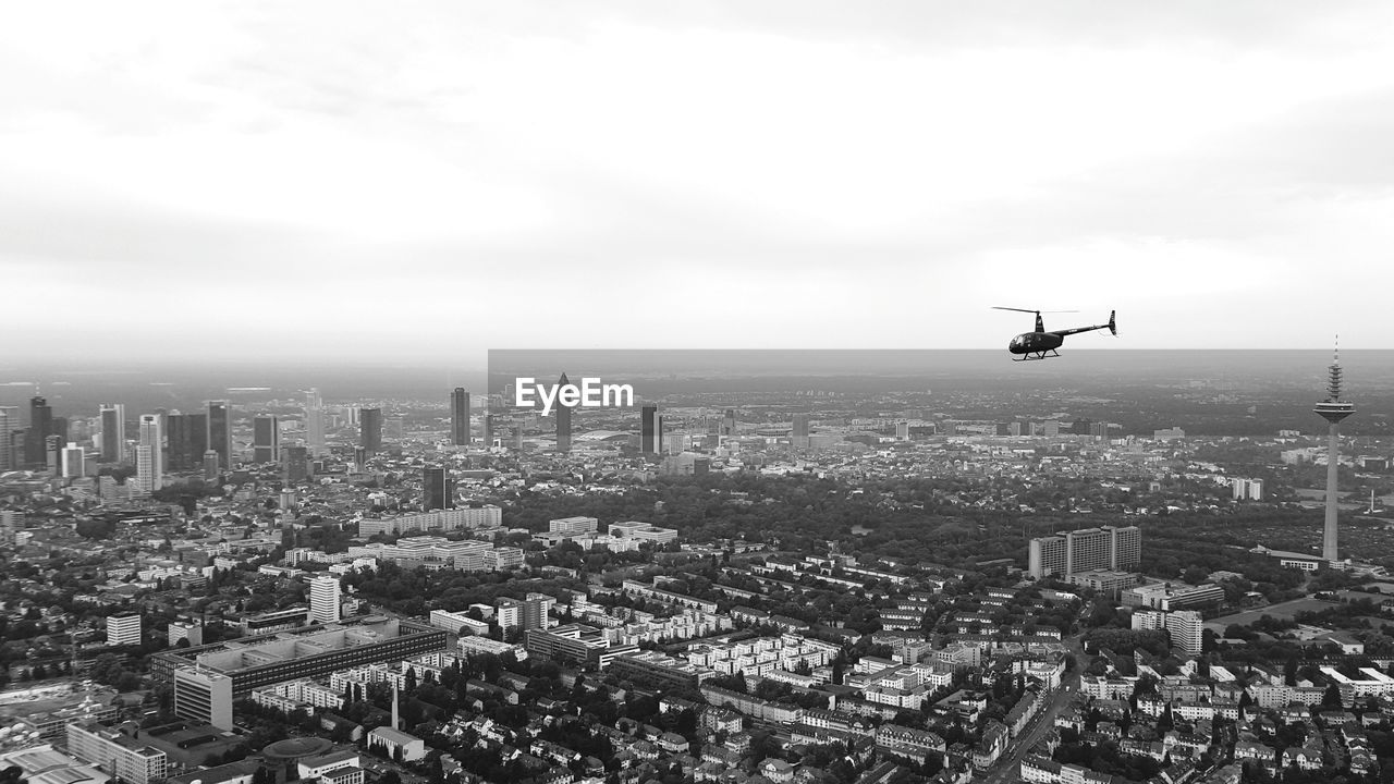 Helicopter flying over cityscape against sky