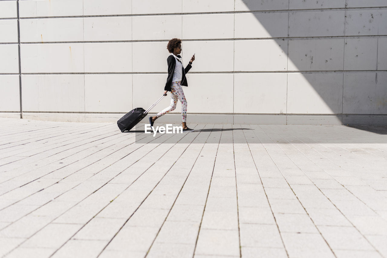 Walking businesswoman with trolley bag looking at her smartphone