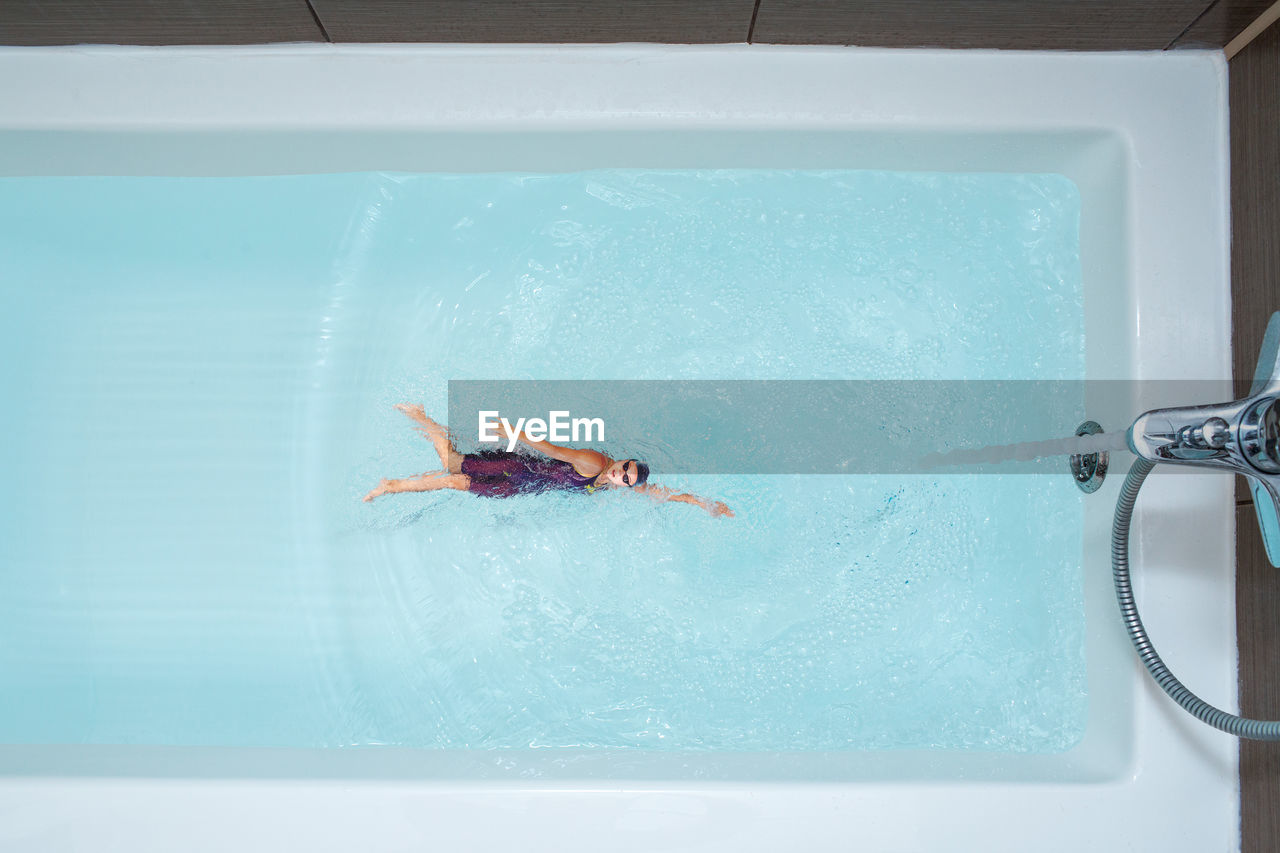 Digital composite image of woman swimming in bathtub