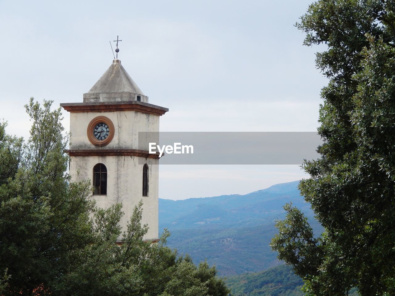 Clock tower by trees with mountains in background against sky