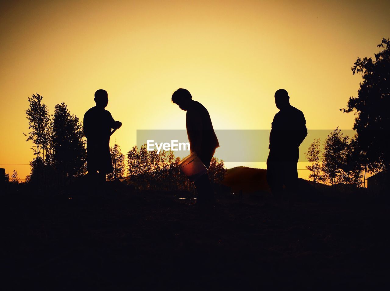 Silhouette people standing on landscape against orange sky