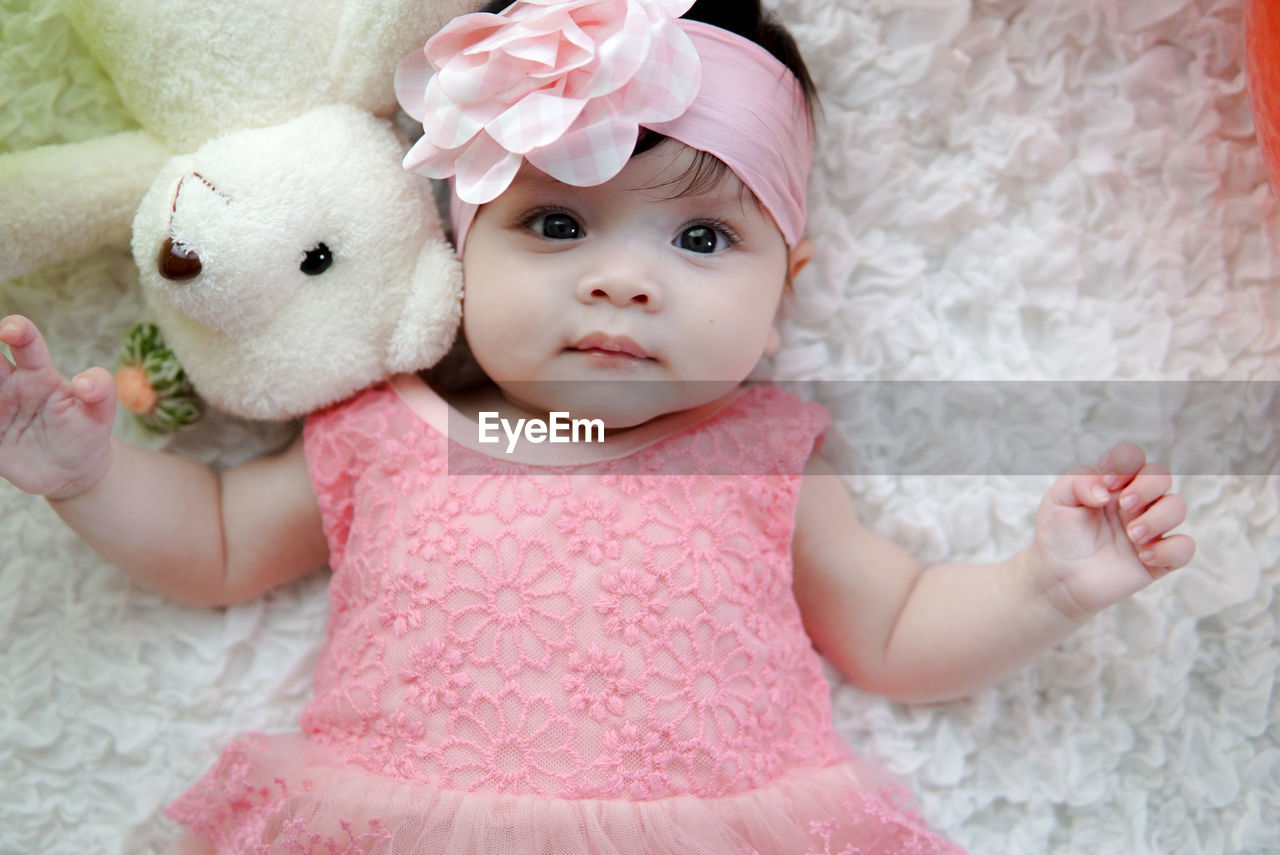 Close-up portrait of baby girl with toys lying on bed