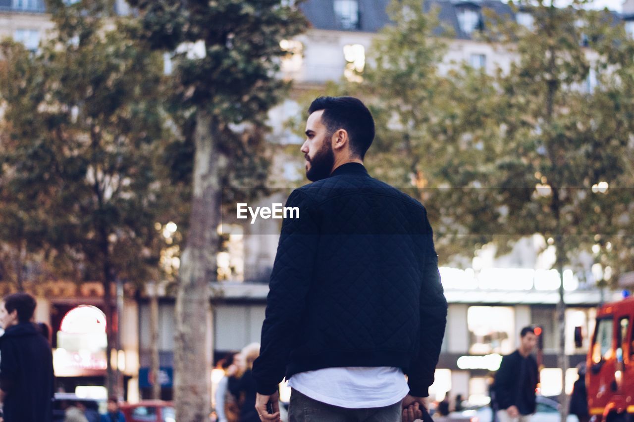 Rear view of man standing against trees in city