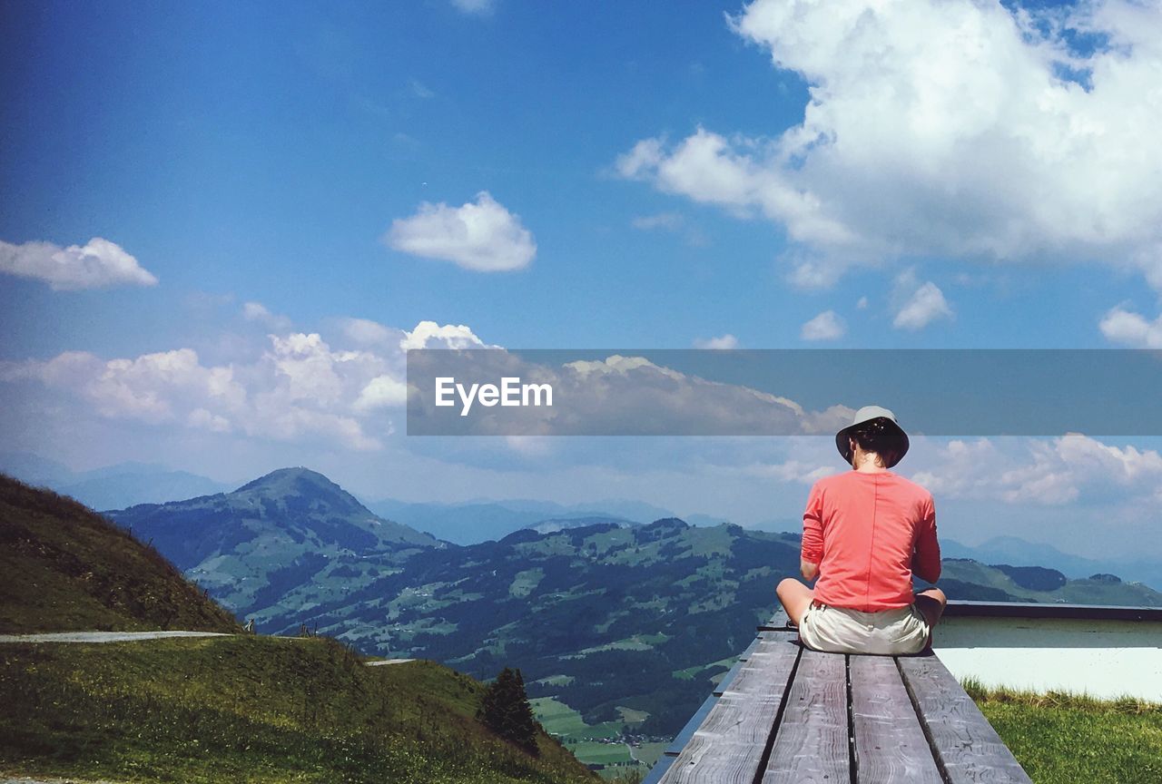 REAR VIEW OF MAN SITTING ON MOUNTAIN