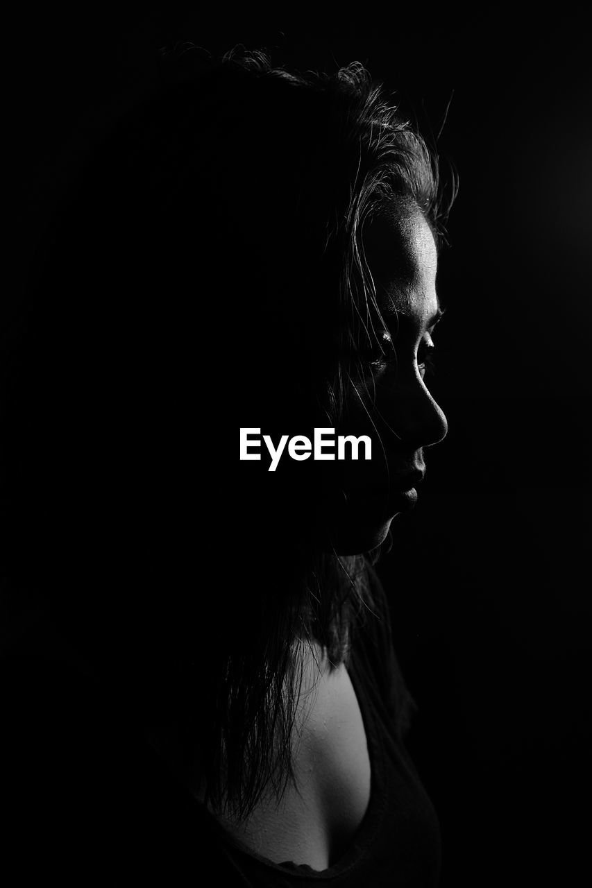 Close-up of sad woman looking away against black background