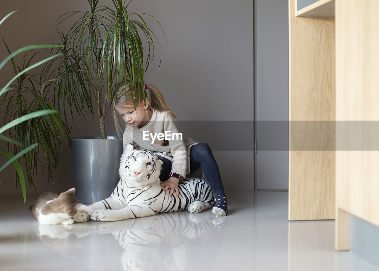 A little girl sits on the floor and holds a cat in her hands