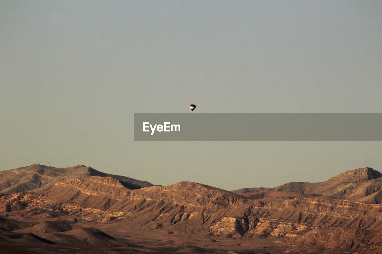 Hot air balloon flying over mountains against clear sky