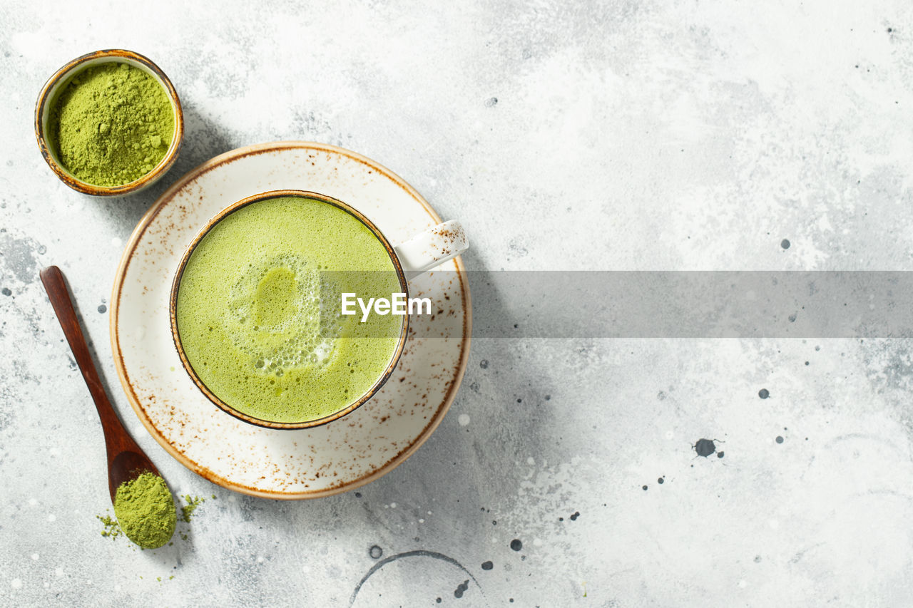 Matcha green tea latte in a cup with cream on a light concrete background. 