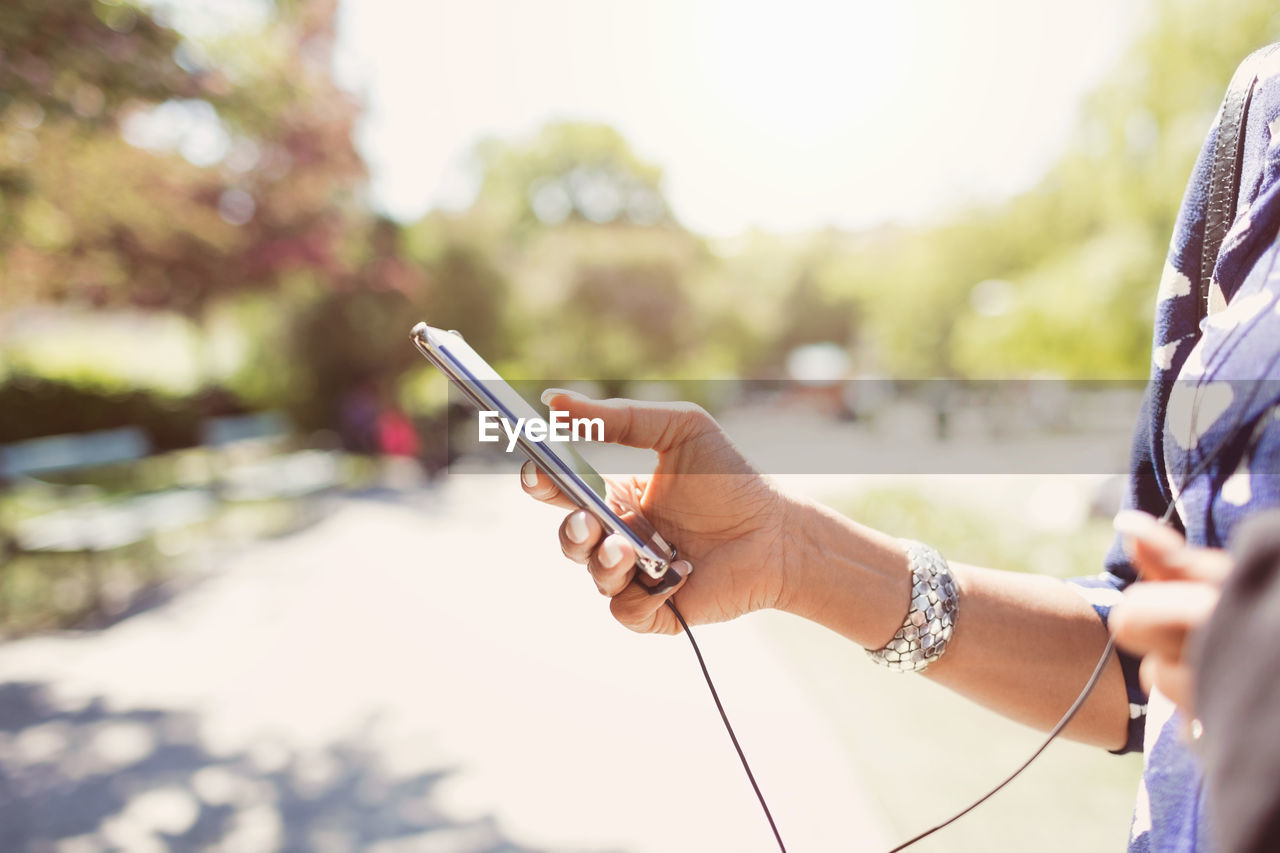 Cropped image of businesswoman holding smart phone on footpath at park