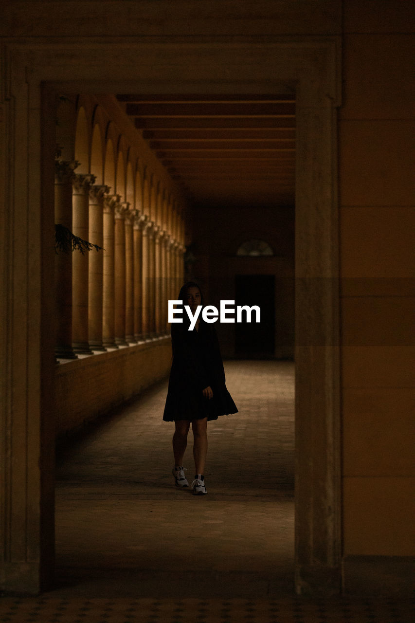 Full length of young woman standing in dark corridor