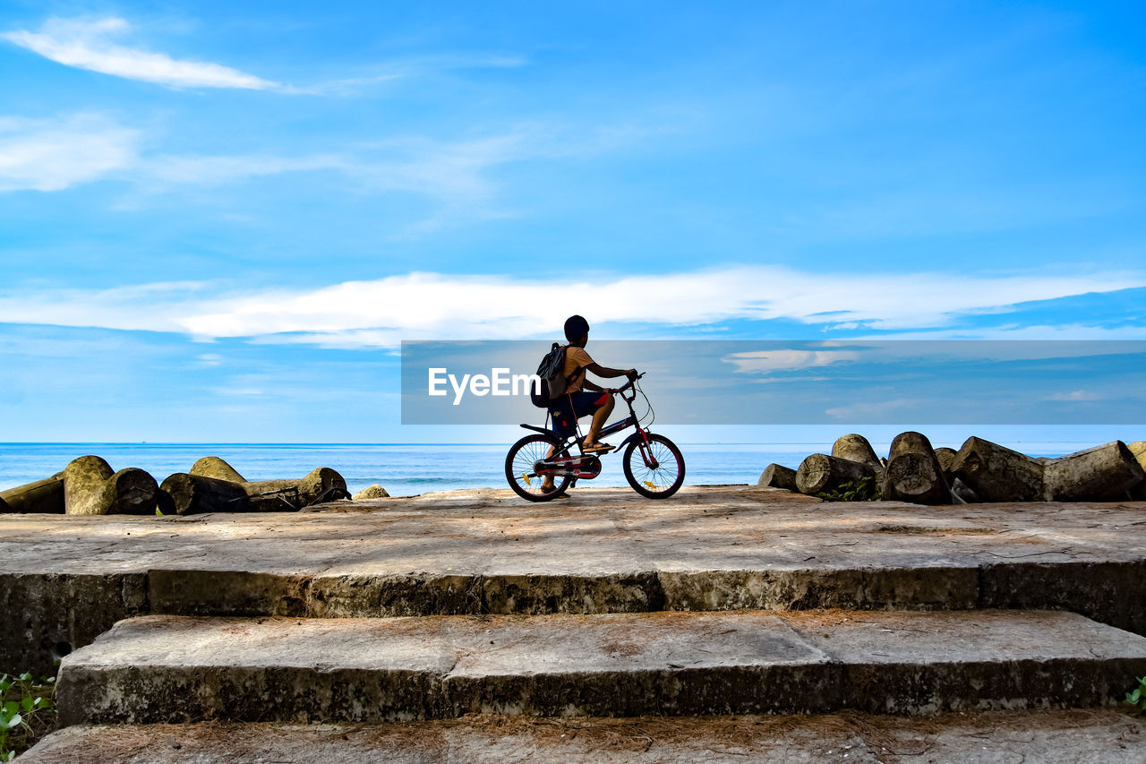 Boy riding bicycle on rocks against sky