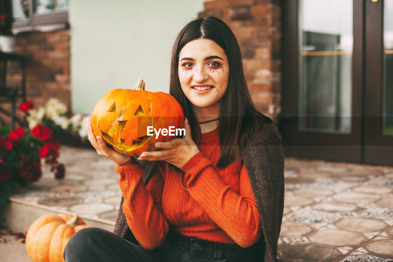A beautiful girl with dark hair with makeup for the celebration of halloween holds a pumpkin