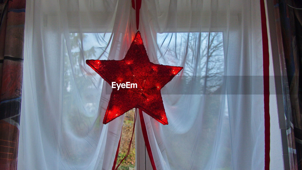 Star shape lighting equipment hanging against white curtain at home