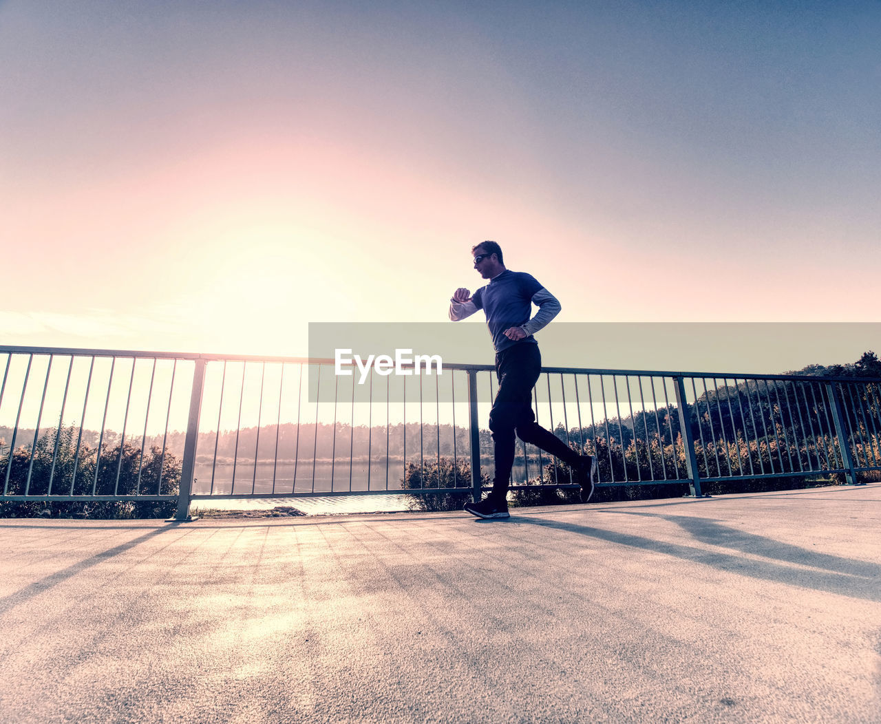 Tall slim man run on the lake terrace against the backdrop of a beautiful sunrise. shore of lake