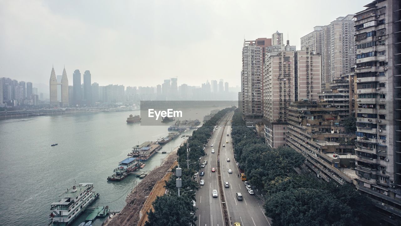 High angle view of city street and buildings by river against sky