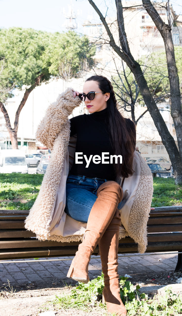 Full length of young woman sitting on bench at park