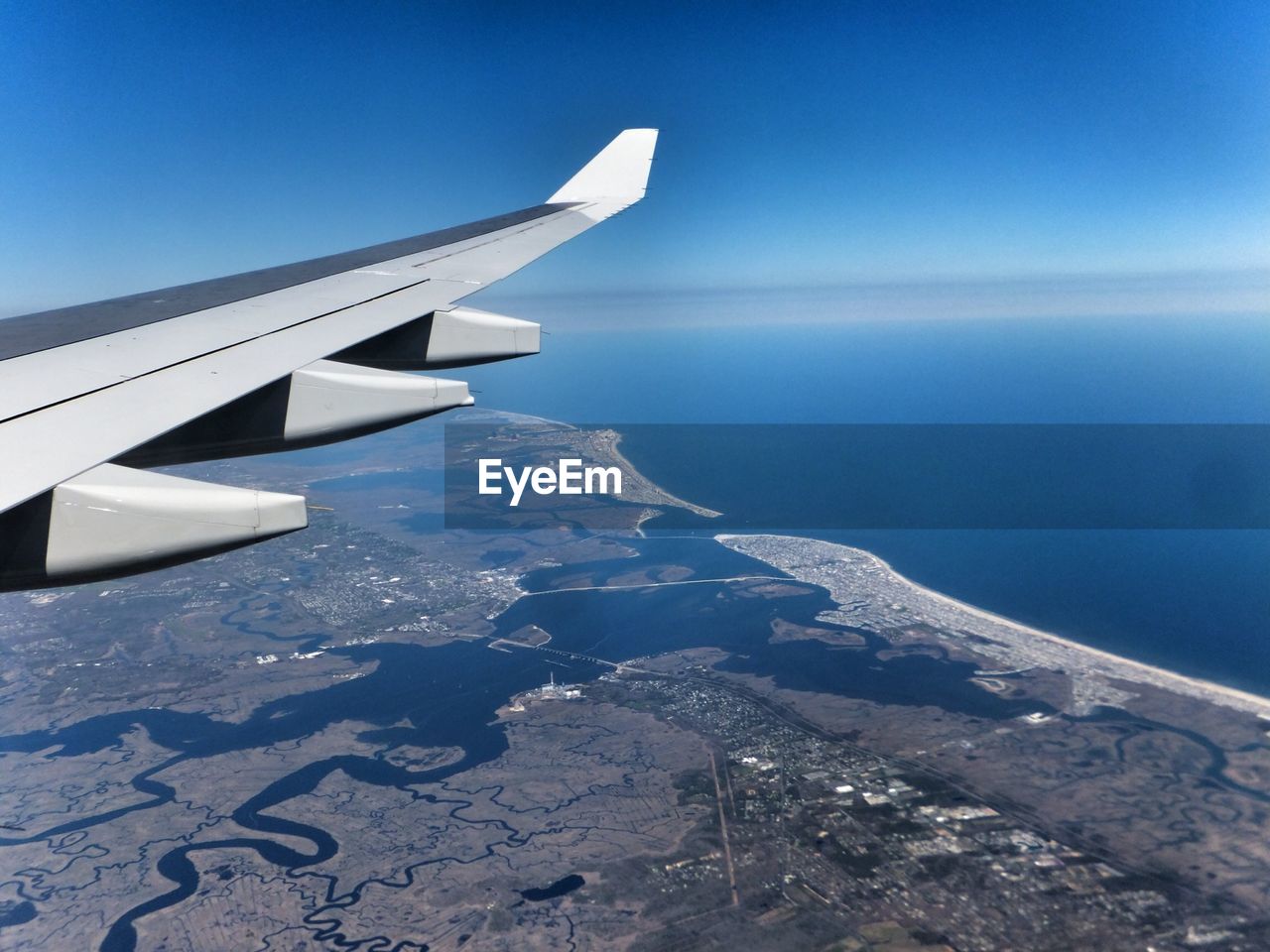 Cropped image of aircraft wing flying over landscape by sea