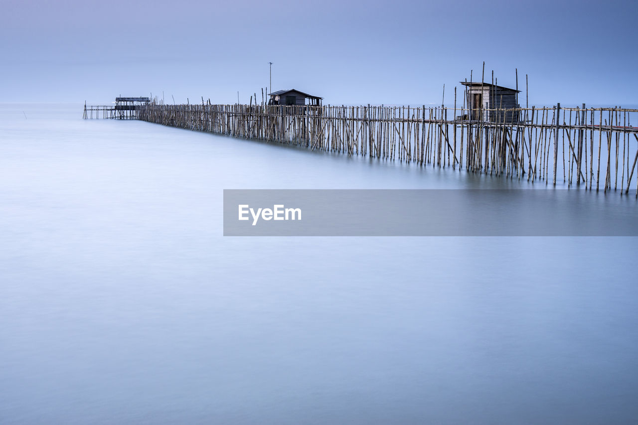 Stilt houses and pier over sea against clear sky