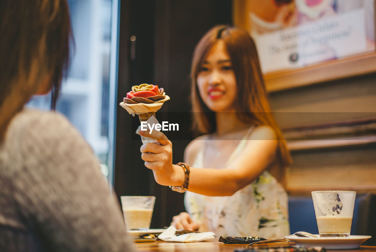 Woman giving ice cream cone to female friend in restaurant