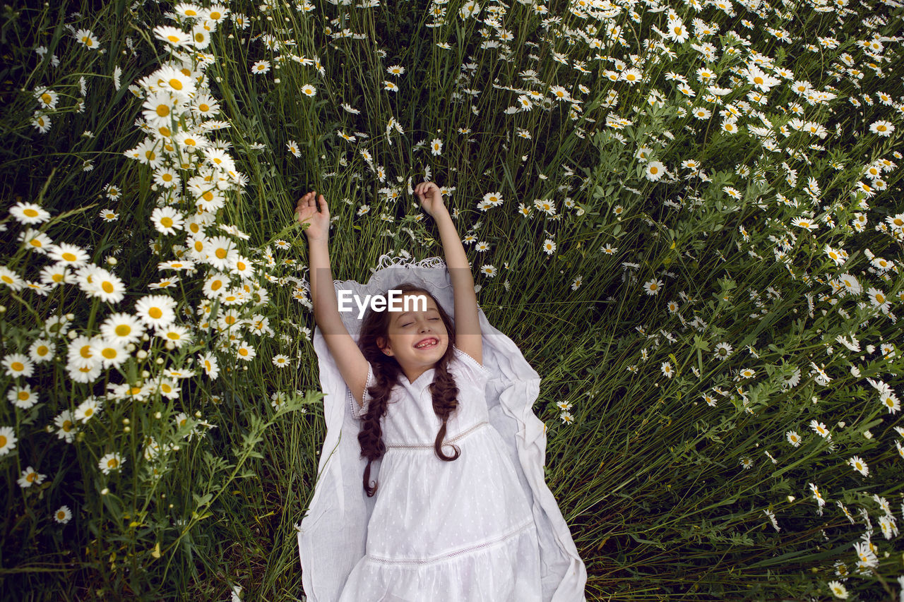 Girl child lies on a camomile field in a white dress in summer