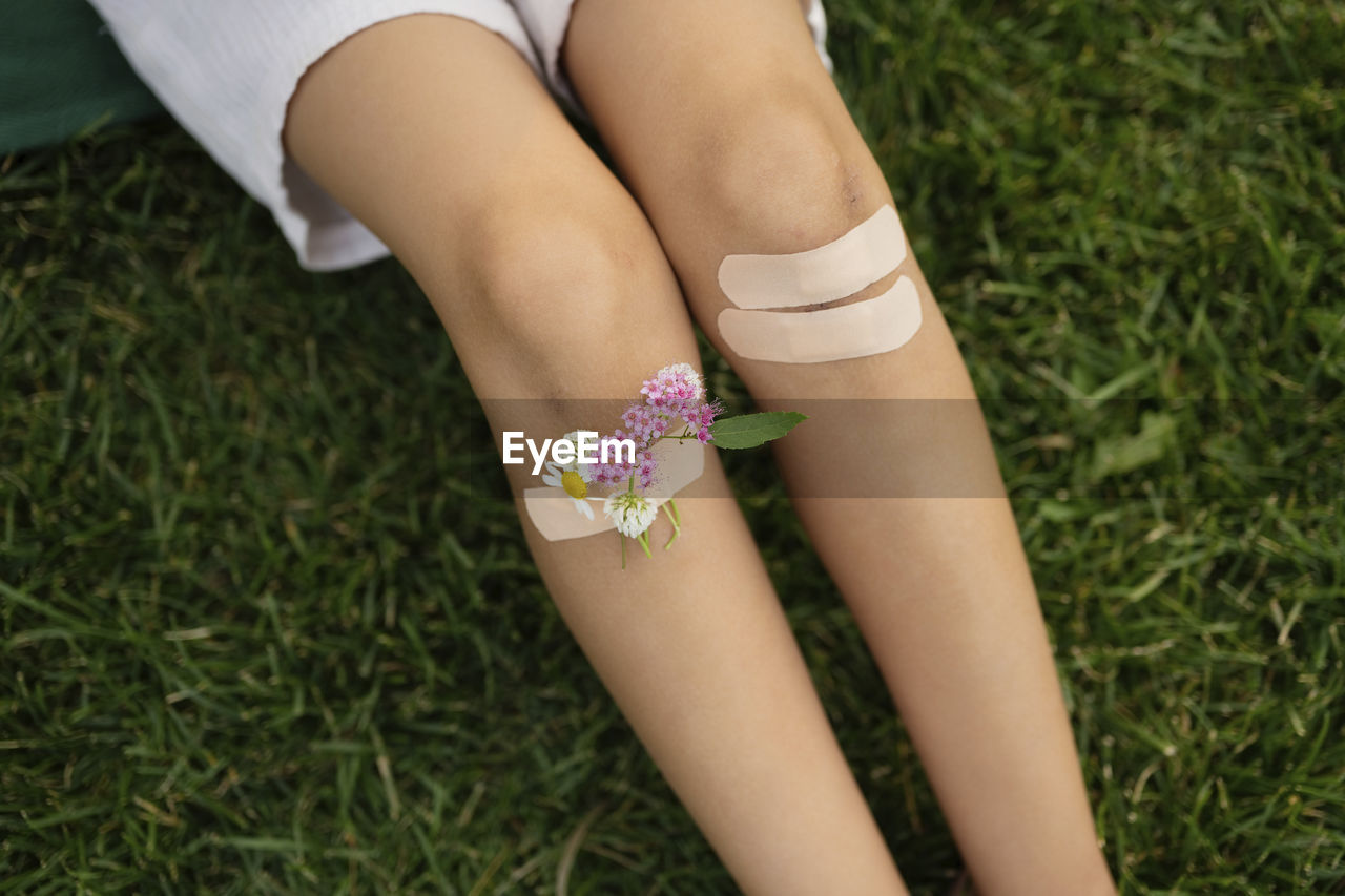 Girl with knees taped by bandage and flowers sitting on grass