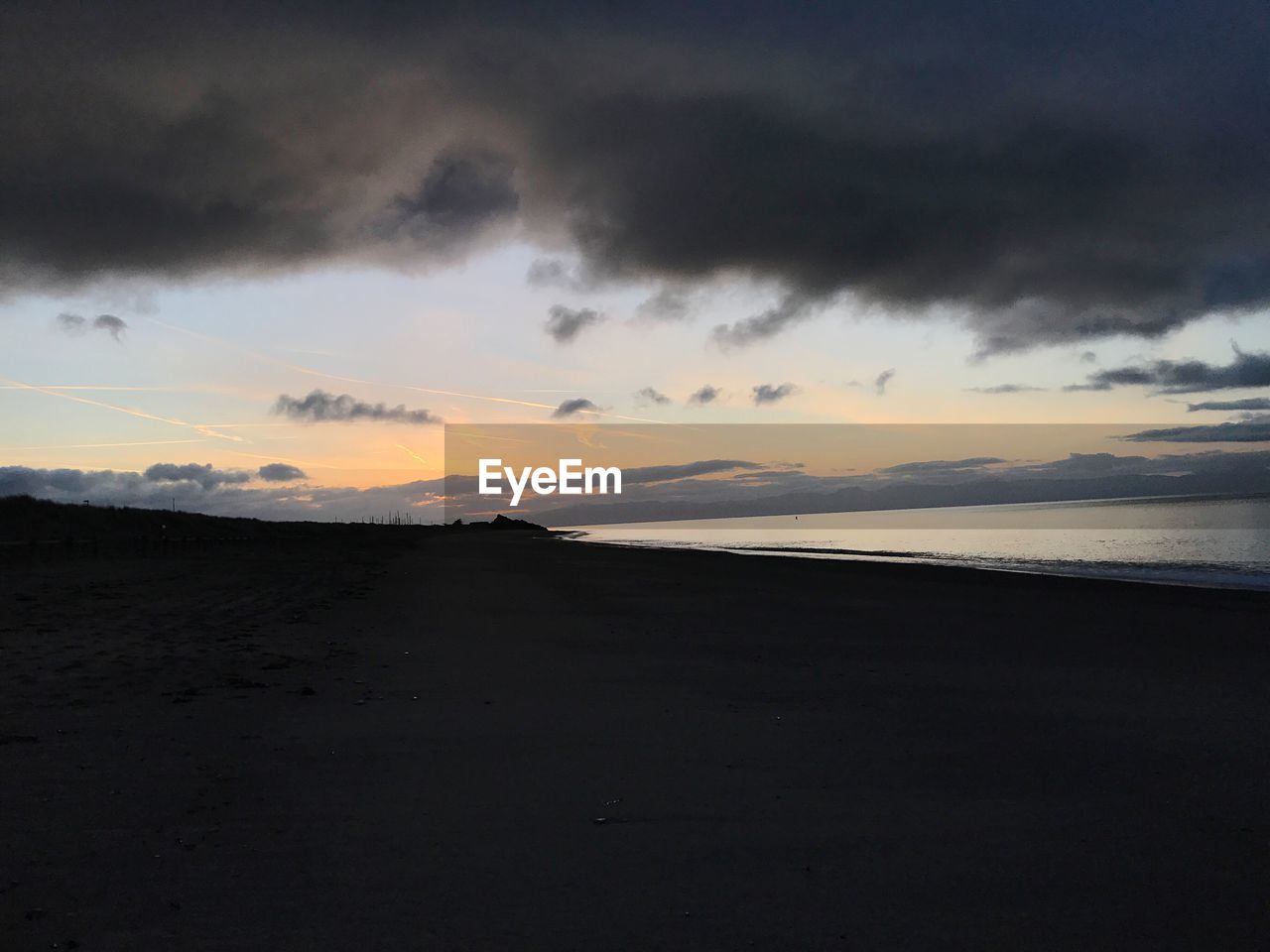 SCENIC VIEW OF BEACH AGAINST DRAMATIC SKY DURING SUNSET