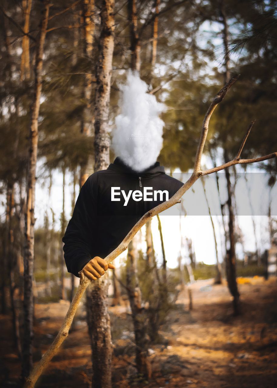 Man standing by tree trunk in forest