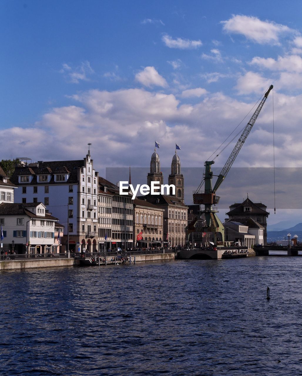 City by river against cloudy sky