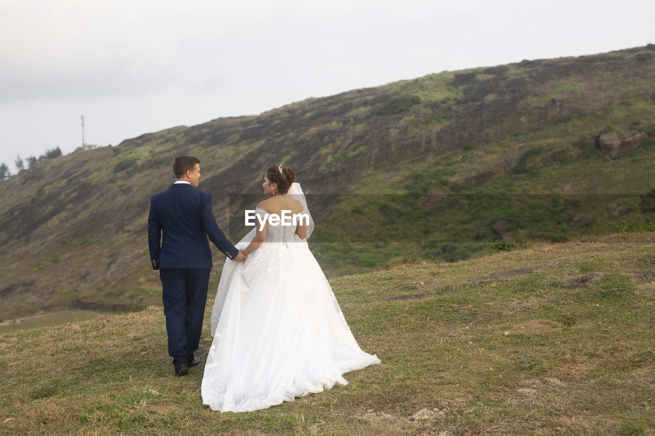 Rear view of bride and groom walking on hillside