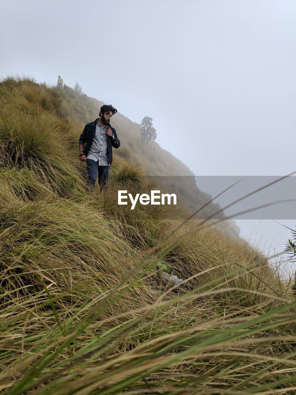 Low angle view of young man standing on grassy mountain against sky