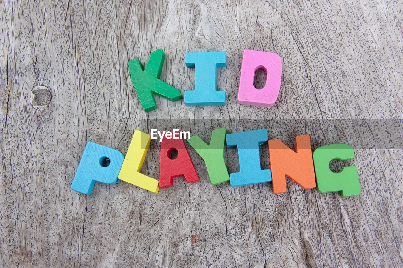 Directly above shot of multi colored alphabet blocks with kid playing wording on wooden background