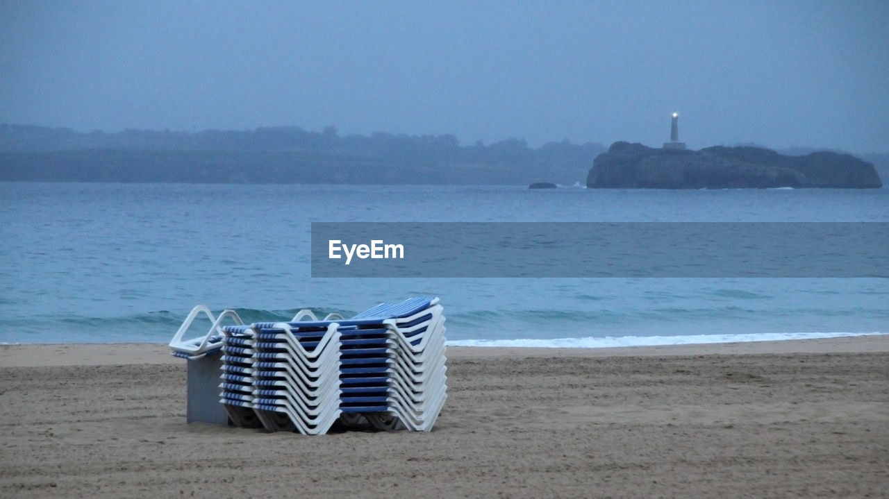 Deck chairs on beach against sky