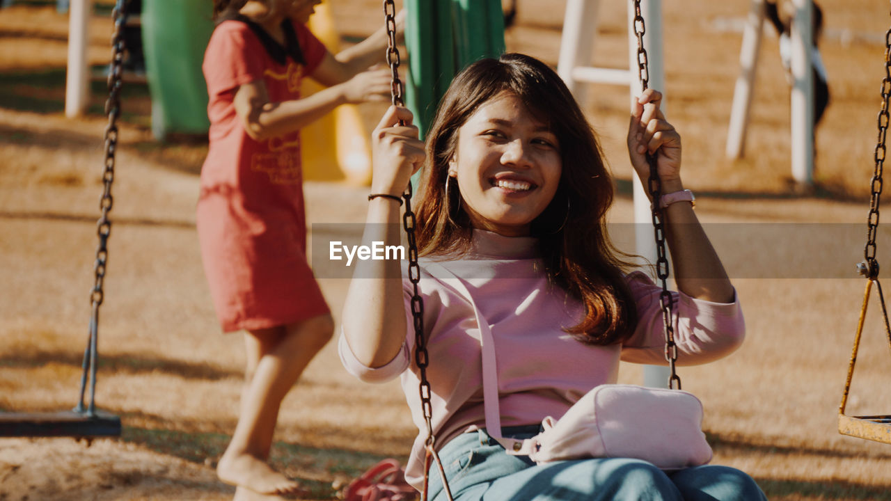 Happy young woman looking away while swinging at park