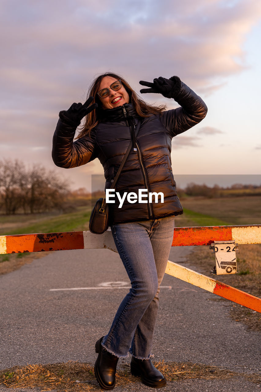 Middle aged woman wearing winter clothes have fun and make victory sign with hands outdoors