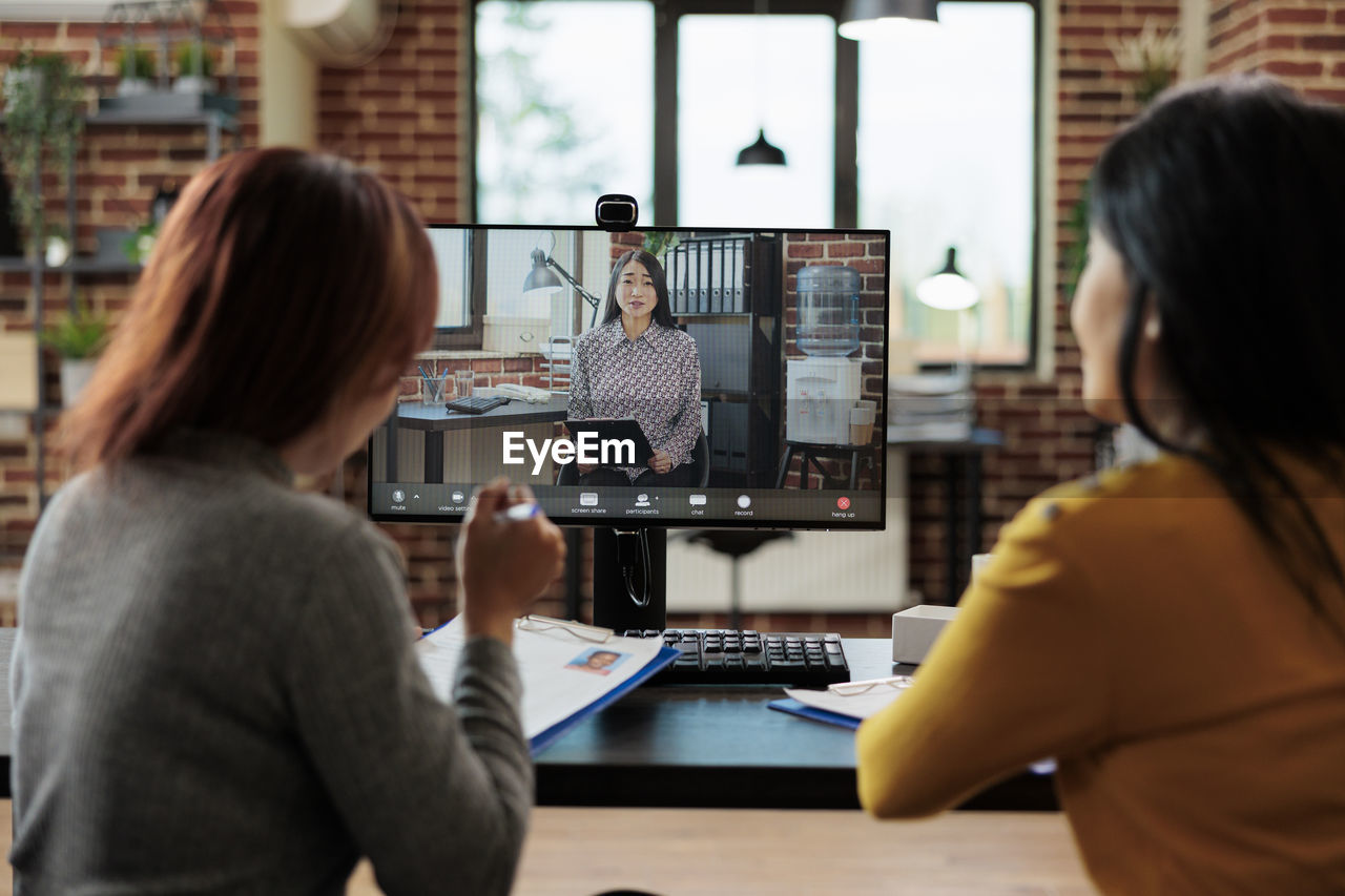 Rear view of businesswomen talking on video call office