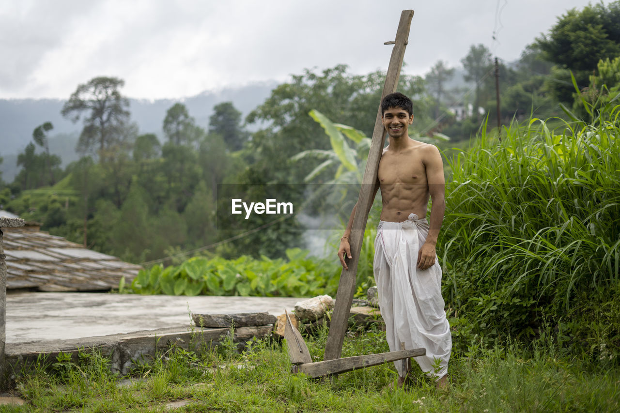 Happy indian farmer standing with wooden plough in rice field