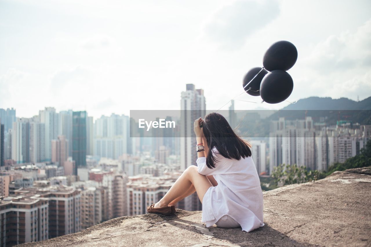 Woman holding black balloons looking at cityscape