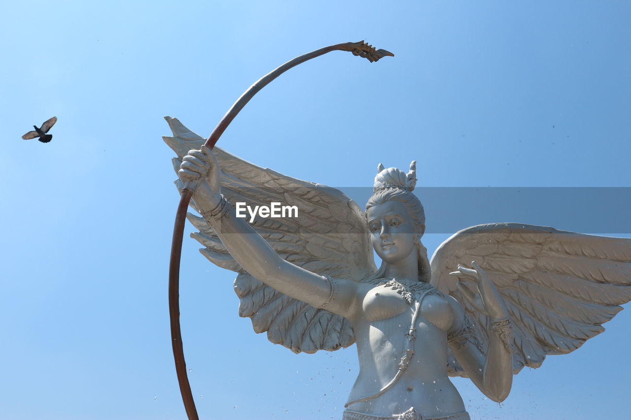 Low angle view of bird flying by statue against clear sky