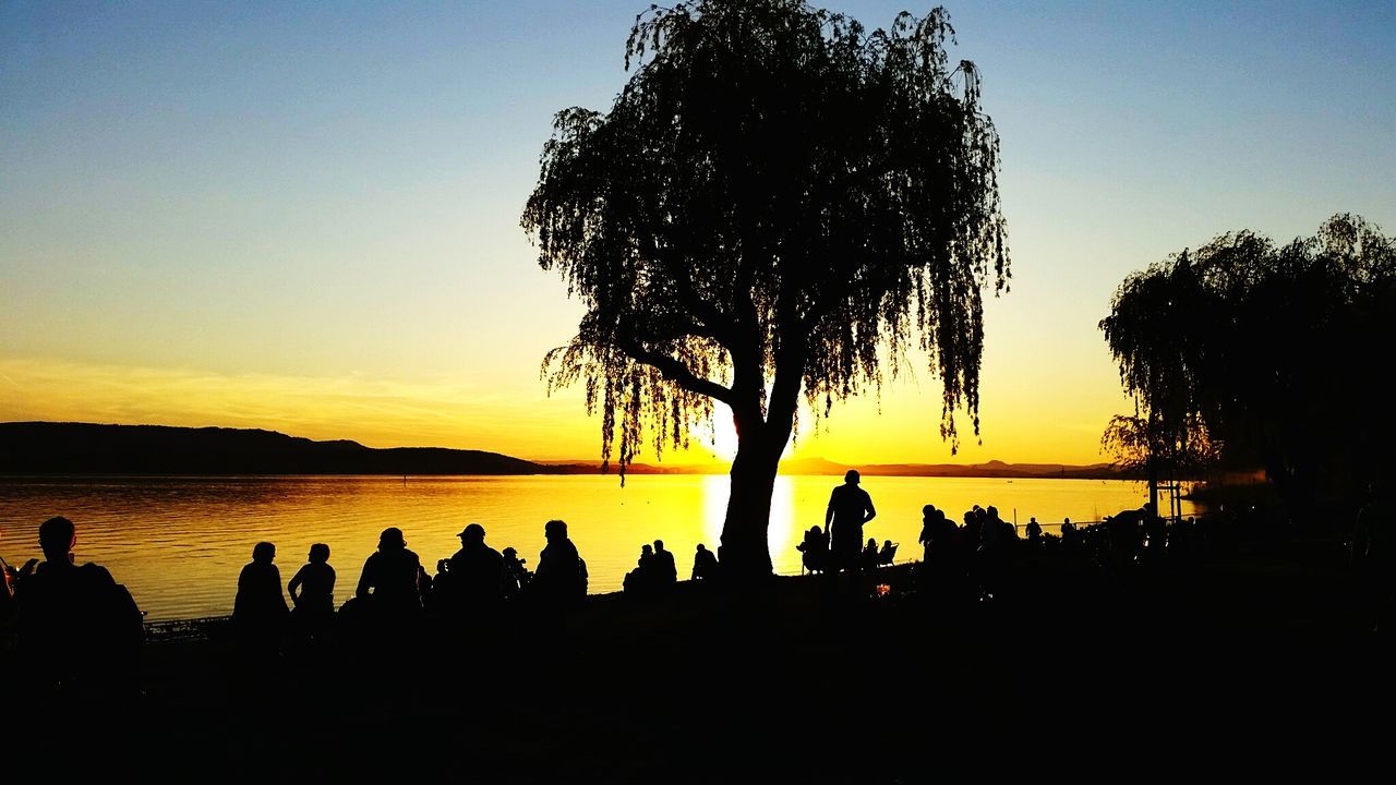 SILHOUETTE PEOPLE BY LAKE AGAINST SKY AT SUNSET