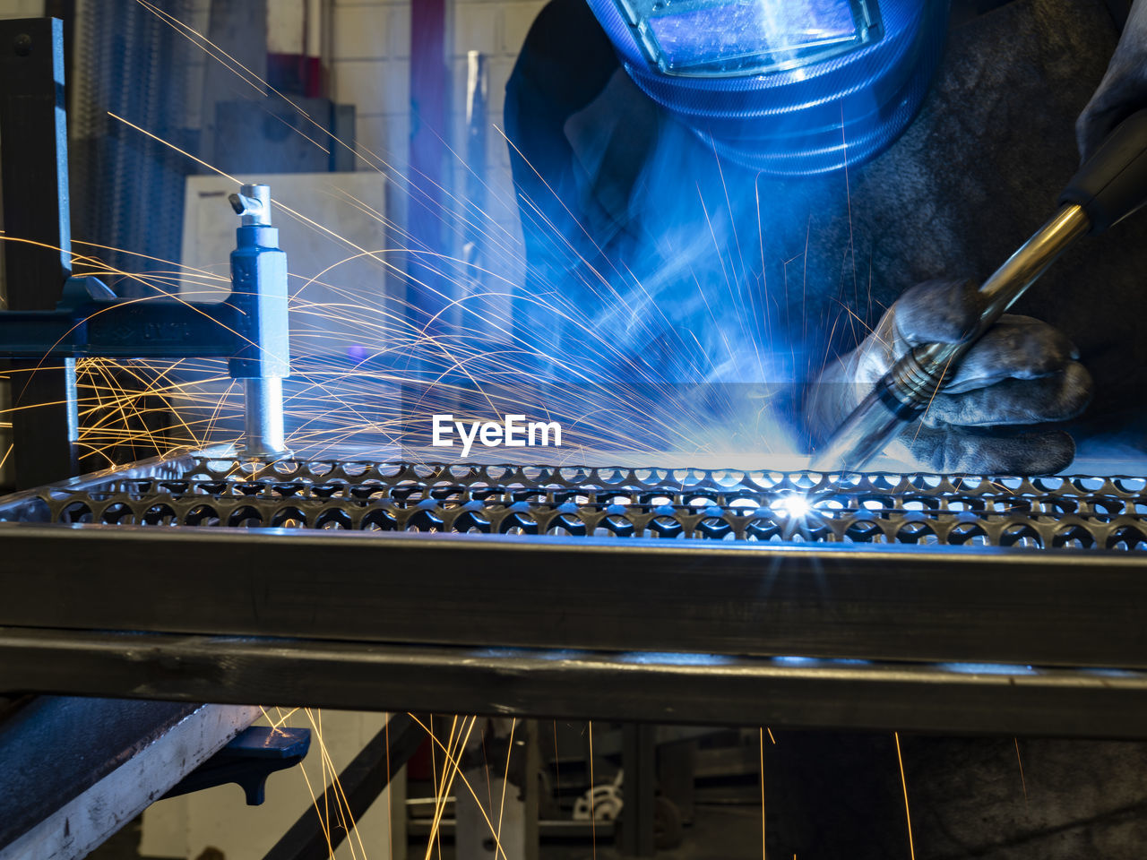 Unrecognizable male welder using welding machine on metal detail while working at workbench in factory