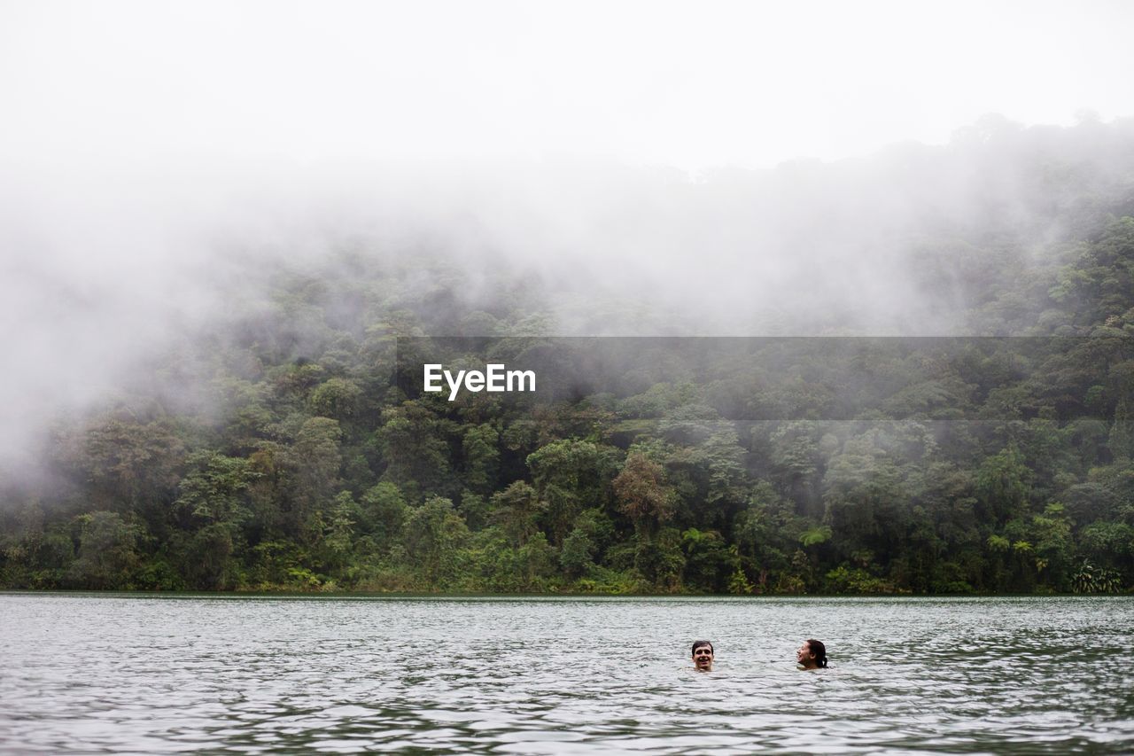 Friends swimming in lake during foggy weather